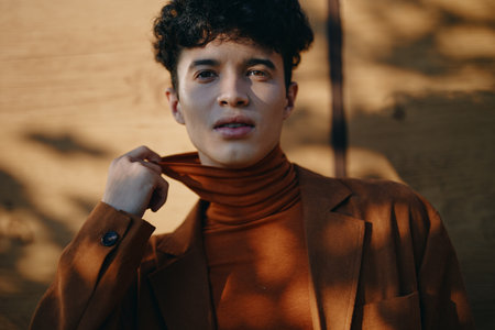 Portrait of a young man in a stylish brown outfit against a wooden background, showcasing confidence and modern fashionの写真素材