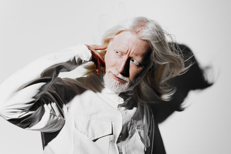 elderly man with long white hair and beard, wearing a white shirt, dramatic pose, shadow effects against a minimalist white background that adds an artistic touch to the imageの写真素材