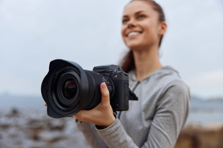 Young woman with a camera smiling at the beach, showcasing passion for photography during a cloudy day Photography, beach, smiling, young woman, camera, passion, cloudyの写真素材