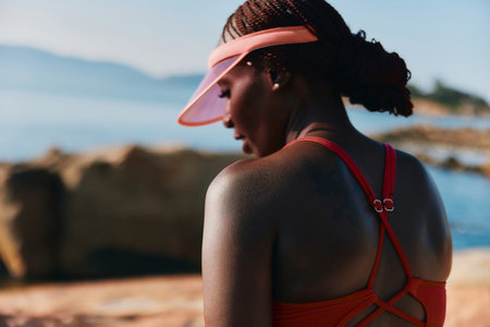 Athletic woman in sporty attire by the seaside during sunlight, showcasing strong physique and...