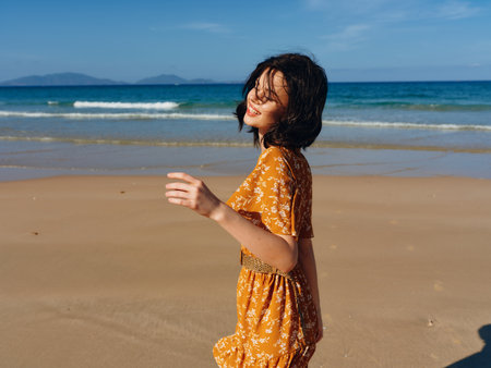 Serene woman in a stylish yellow dress standing calmly on the sandy beach with her hands casually tucked in her pocketsの写真素材