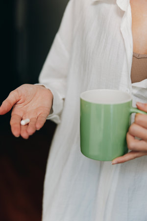 Woman holding green coffee mug and pill in handの写真素材