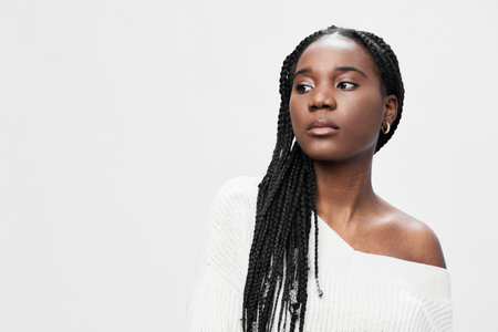 Confident young woman with braided hair wearing a white off shoulder sweater, exuding elegance...
