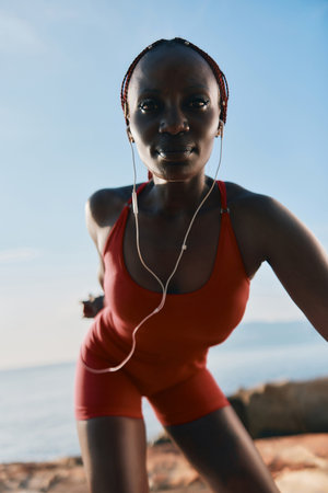 Athletic woman jogging by the sea in a red workout outfit with earphonesの写真素材