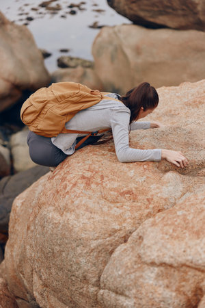 Young woman with brown backpack climbing on rocky terrain, showcasing determination and adventure in a natural outdoor settingの写真素材