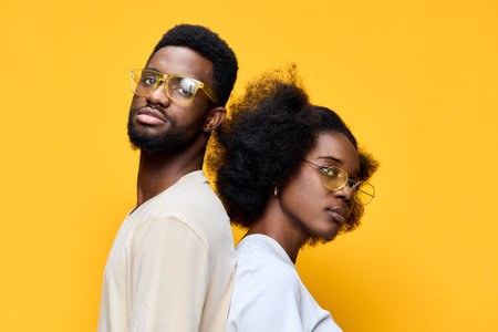 Young couple with stylish glasses posing against a bright yellow background, showcasing modern fashion and confidence in a vibrant, youthful atmosphereの写真素材