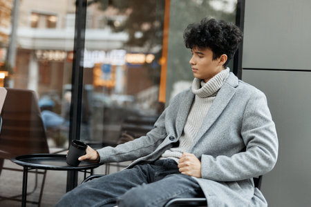 Young man sitting in front of window, holding coffee cup and phoneの写真素材