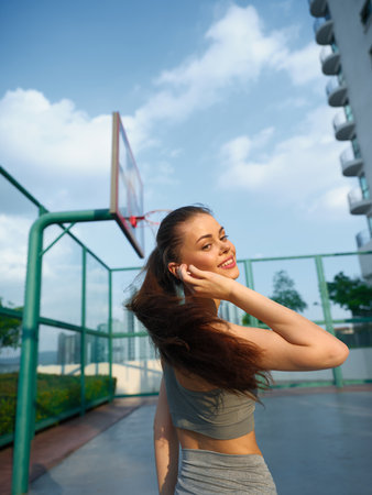 Young woman smiling and looking back while playing basketball outdoors against a blue skyの写真素材