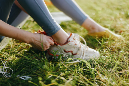 Female athlete tying shoelaces in a grassy field, wearing sporty clothing, showcasing focus and...