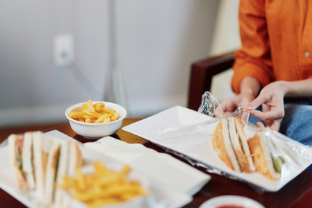 Healthy eating concept with a close up of a person unpacking sandwiches and fries on a table, highlighting fresh ingredients and a casual dining atmosphereの写真素材
