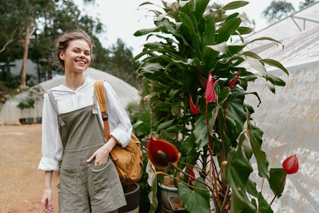 Young woman smiling in trendy overalls, walking among tropical plants in a greenhouse, showcasing joy and nature's beauty in vibrant colorsの写真素材
