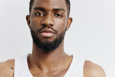 Confident african american man with beard in white tank top posing against clean white backgroundの写真素材