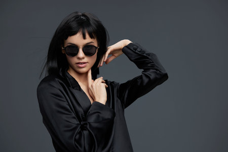 Woman in sunglasses and black blouse poses for camera against gray background, exuding confidence...