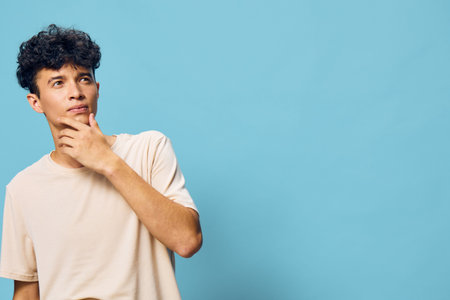 Young man thinking on a blue background, casual attire, pondering expression Ideal for concepts of...