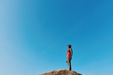 Woman standing confidently on a rocky outcrop against a clear blue skyの写真素材