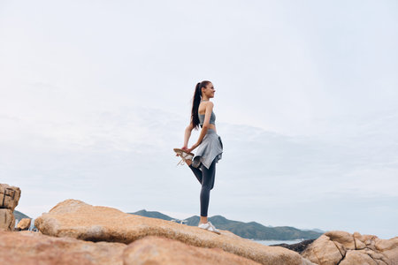 Young woman practicing yoga on rocky terrain, showcasing strength and flexibility in sporty attire, embodying a healthy lifestyle and tranquilityの写真素材