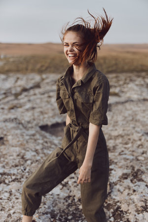 Woman in olive green jumpsuit standing on rock with blowing hair beauty and fashion in nature environmentの写真素材