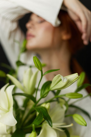 Elegant young woman with long hair holding a bouquet of white lilies, expressing a serene emotion against a dark backgroundの写真素材