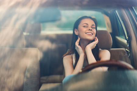 Young woman smiling in a car, enjoying the moment with a relaxed and happy expression in a sunny setting, emphasizing joy and freedom.の写真素材