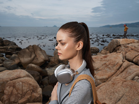 Young woman with headphones on rocky beach, demonstrating relaxed mood and scenic ocean view, perfect for themes of leisure, travel, and escapismの写真素材