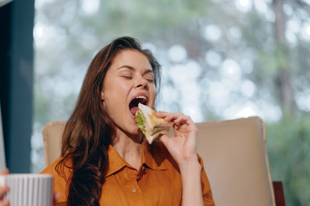 Young woman enjoying a healthy sandwich in a cozy setting, highlighting a lifestyle of healthy eating and wellnessの写真素材