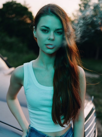 Young woman with long hair in casual outfit expressing confidence, standing by a car in a greenish background, capturing the essence of modern lifestyle and freedom.の写真素材