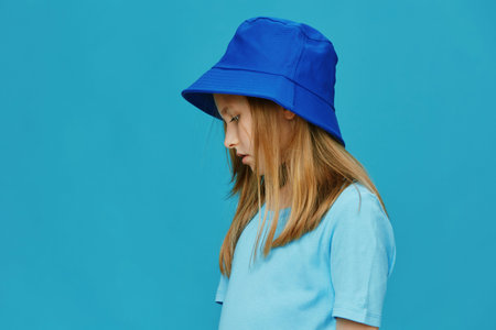 Profile of a young girl wearing a blue bucket hat and a matching t shirt against a turquoise background, conveying a calm, thoughtful emotionの写真素材