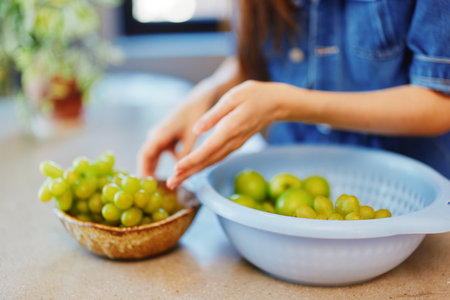 Woman harvesting ripe green grapes from a bowl in front of a tempting display of fresh fruitの写真素材