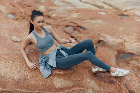 Young athletic woman in sportswear relaxing on rocky terrain, showcasing healthy lifestyle and...