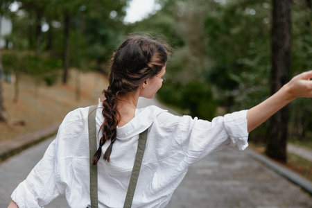 Young woman in casual outfit expressing freedom, with braided hair, walking in nature on a sunny day...