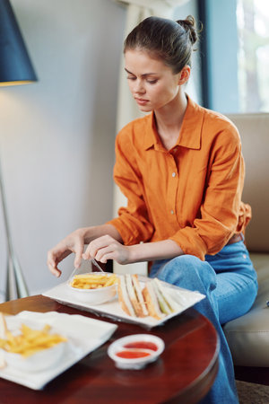 Young woman in an orange shirt enjoying a healthy meal of sandwiches and fries in a modern caf setting, reflecting a lifestyle of healthy eatingの写真素材