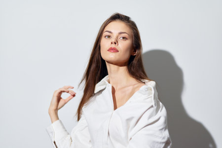 Portrait of a confident young woman with long hair in a white shirt against a light background, showcasing elegance and poise in a minimalist styleの写真素材