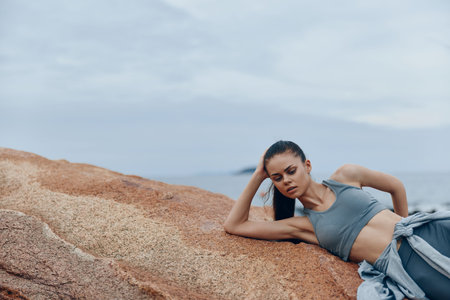 Young athletic model in sportswear relaxing on rocky beach, capturing the essence of fitness, serenity, and tranquility in a natural coastal settingの写真素材