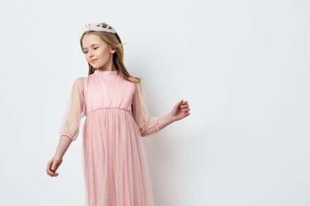 A young girl wearing a pink dress with tulle sleeves poses gracefully against a light background, exuding innocence and beauty, perfect for spring themed photographyの写真素材