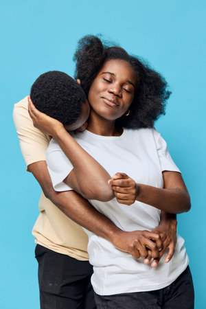 A joyful couple embracing each other against a vibrant blue background, showcasing love and connection while wearing casual outfitsの写真素材