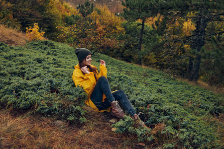 A serene woman wearing a bright yellow coat relaxing on the hillside in the peaceful forest nature