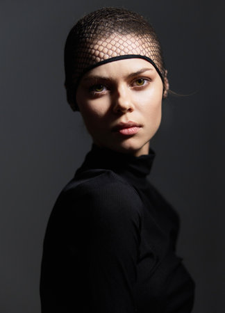 Confident young woman with short hair wearing a black outfit and a fishnet headpiece. Dramatic lighting enhances her strong expression and fierce demeanor.の写真素材