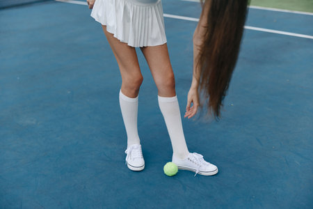 Young female athlete in white tennis attire plays on a court, showcasing white socks and sneakers,...