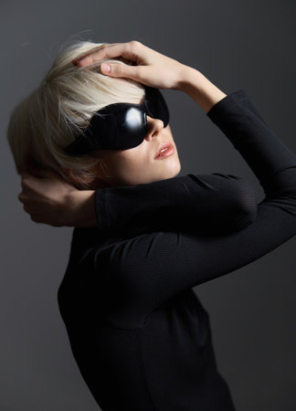 Stylish European woman with short blonde hair wearing oversized black sunglasses, striking a confident pose against a dark background. Fashion and elegance concept.の写真素材