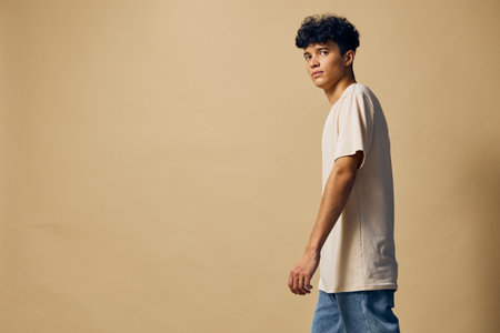 Young man in casual outfit walking against a plain beige background, showcasing modern fashion trends and relaxed style, ideal for lifestyle and fashion imageryの写真素材