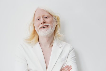 Smiling man with long white hair and beard in a white suit against a light, neutral background, exuding confidence and positivity in a minimalistic settingの写真素材