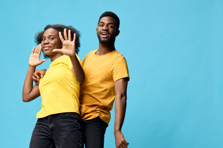 Young African couple celebrating joyfully in matching yellow outfits against a bright blue...