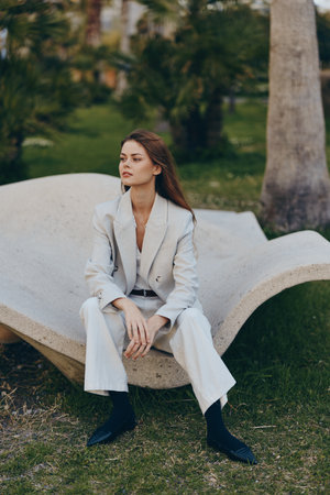 Woman in light beige business suit sitting outdoors in modern chair during spring, confident young Caucasian woman in elegant fashion, professional attire and stylish lookの写真素材