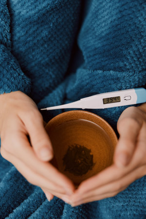 Person holding thermometer and drinking tea in a chair