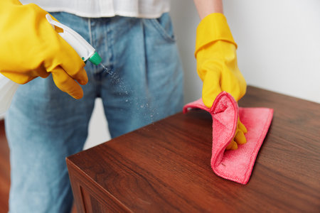 Woman in yellow gloves cleaning wooden table with rag and cleaning solution