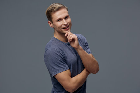 smiling young caucasian man in blue t-shirt thinking pose look camera isolated on grey background digital nomad lifestyle conceptの写真素材