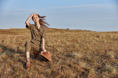 Woman sitting in field with hands on head and hat in travelinspired fashion beauty shot in natureの写真素材