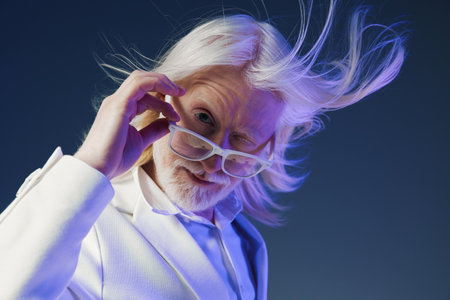 Portrait of a stylish elderly man with long white hair and glasses, wearing a white suit against a dark gradient background, creating a modern and sophisticated atmosphereの写真素材