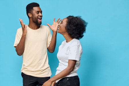 Joyful young African American couple celebrating with excited expressions against a bright blue background, showcasing happiness and connection in casual outfitsの写真素材