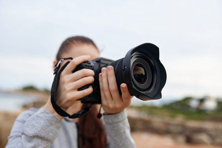 Young woman capturing scenic views with a professional camera, expressing creativity and enthusiasm in a natural outdoor setting, ideal for photography concepts and inspirationの写真素材